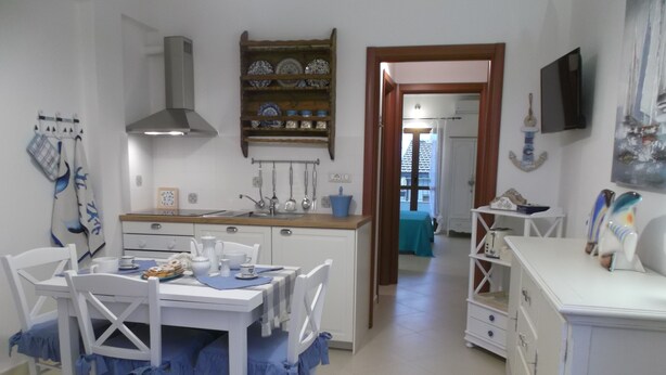 Une cuisine moderne avec des meubles blancs, un îlot central et un coin repas avec des chaises blanches et des nappes bleues.