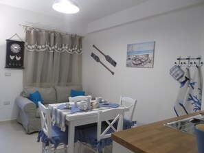 A dining area with a table set for two, a sofa, and a kitchen counter.