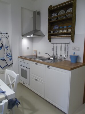 A compact kitchen with white cabinets, a wooden countertop, a built-in oven, a stainless steel sink, and a range hood.