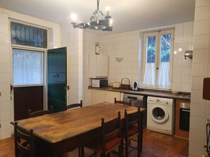 A compact kitchen with a wooden table, a washing machine, and a window with curtains.