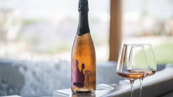A bottle of wine and a glass on a table by a window.