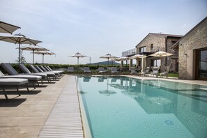 Una piscina con sillas de descanso y sombrillas, rodeada de edificios de piedra con balcones.