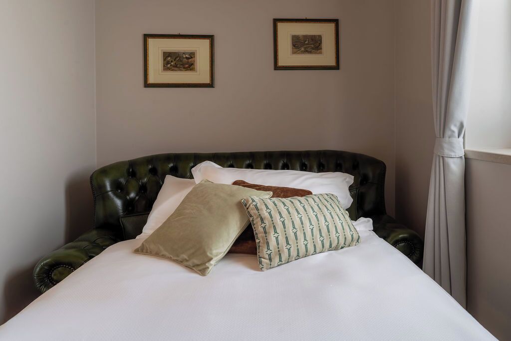 A bed with a dark headboard, white bedding, and two pillows. There are two framed pictures on the wall above the bed.