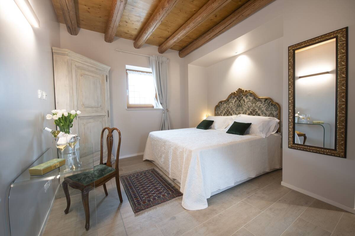 A bedroom with a bed, a chair, a desk, a mirror, and a window with curtains.