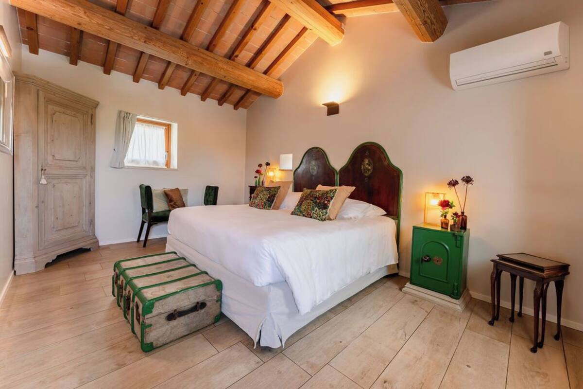 A bedroom with a wooden ceiling, a bed with white bedding, a green nightstand, and a small table.