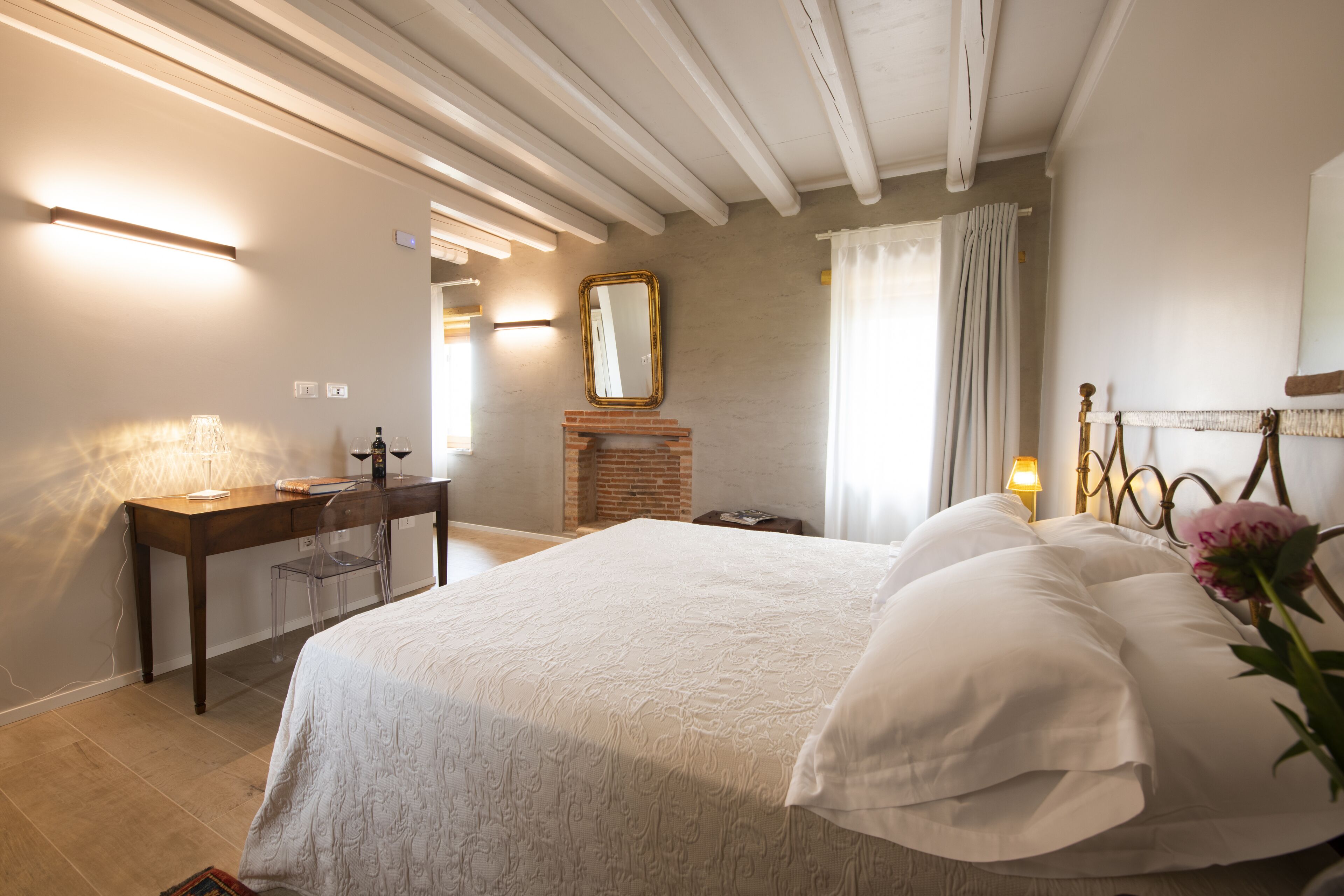 A bedroom with a bed, bedside table, lamp, mirror, and a fireplace.