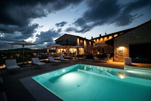 A swimming pool with lounge chairs and umbrellas, a stone building with outdoor seating, and a view of the sky. - Magari Estates Hotel (Colognola ai Colli)