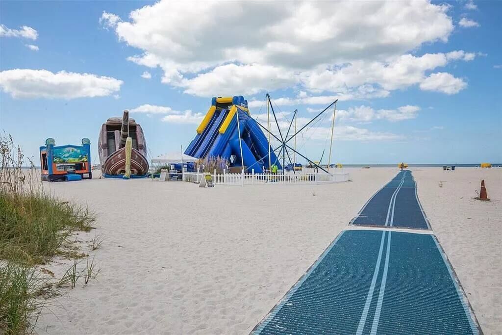 A beach with a blue running track, a large inflatable slide, and a boat-shaped structure.