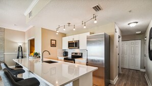 A modern kitchen with a central island, stainless steel appliances, and a bar seating area. - Breathtaking Gulf View ~ 2min to Beach ~ Pool ~ Pkg (Treasure Island)