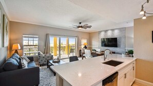 A modern kitchen with a large island, a dining area with a table and chairs, and a living room with a sofa and a TV. - Breathtaking Gulf View ~ 2min to Beach ~ Pool ~ Pkg (Treasure Island)