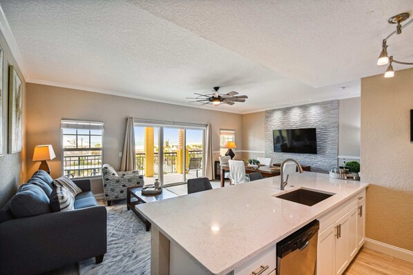 A modern kitchen with a large island, a dining area with a table and chairs, and a living room with a sofa and a TV.