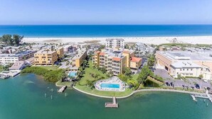 An aerial view of a coastal hotel with multiple buildings, a swimming pool, and a beach in the background. - Breathtaking Gulf View ~ 2min to Beach ~ Pool ~ Pkg (Treasure Island)
