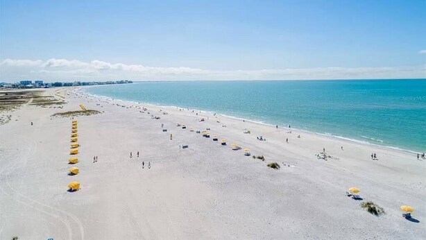 A wide beach with rows of yellow umbrellas and a clear blue sky. - Breathtaking Gulf View ~ 2min to Beach ~ Pool ~ Pkg (Treasure Island)