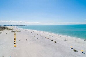 Une vaste plage bordée de rangées de parasols jaunes, sous un ciel bleu et dégagé.