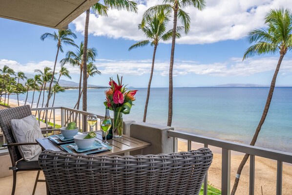 Varanda com mobiliário de vime, uma mesa com um vaso de flores e vista para a praia e o oceano.