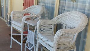 Un espacio de estar techado al aire libre con sillas de mimbre y una puerta roja.