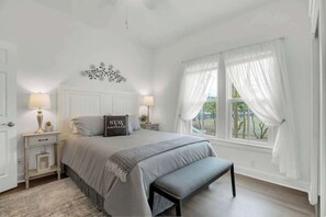 Un dormitorio con cama, mesitas de noche, un banco, una ventana con cortinas y un elemento decorativo en la pared.