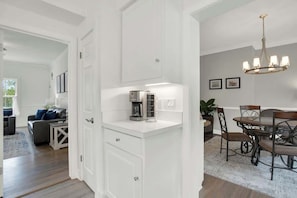 A modern kitchen with white cabinetry, a coffee maker, and a dining area with a chandelier.