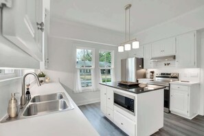 A modern kitchen with white cabinetry, a stainless steel sink, an island with a built-in oven, and a pendant light.