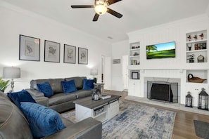A living room with a grey sofa, blue cushions, a coffee table, a fireplace, and a TV on the wall.