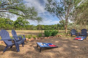 An outdoor seating area with Adirondack chairs and a table with a star design, surrounded by trees and a fence.
