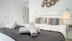 Moderni hotellihuone, jossa on siististi pedattu sänky, seinälle kiinnitetty koristeellinen peili ja selkeä, minimalistinen sisustus.