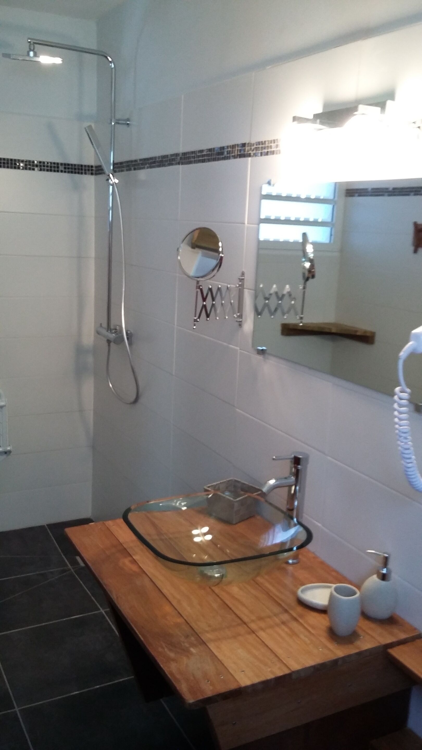 A bathroom with a glass sink, a handheld showerhead, a mirror, and a towel rack.