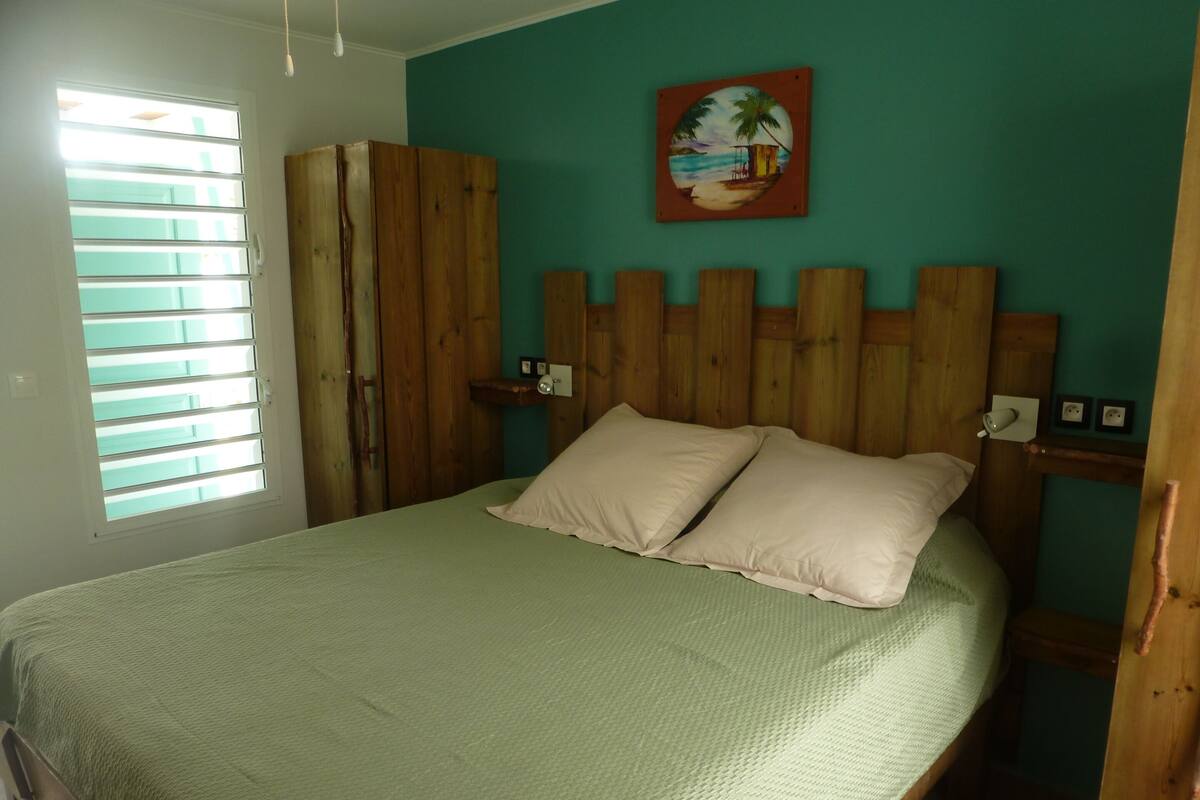 Una habitación con cama, cabecero de madera, una ventana con persianas y un cuadro en la pared.