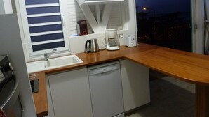 Cocina compacta con lavamanos, cafetera, tostadora y ventana con persianas.