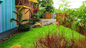 Un espacio al aire libre colorido con césped, una terraza de madera y una estructura de toldo amarillo.