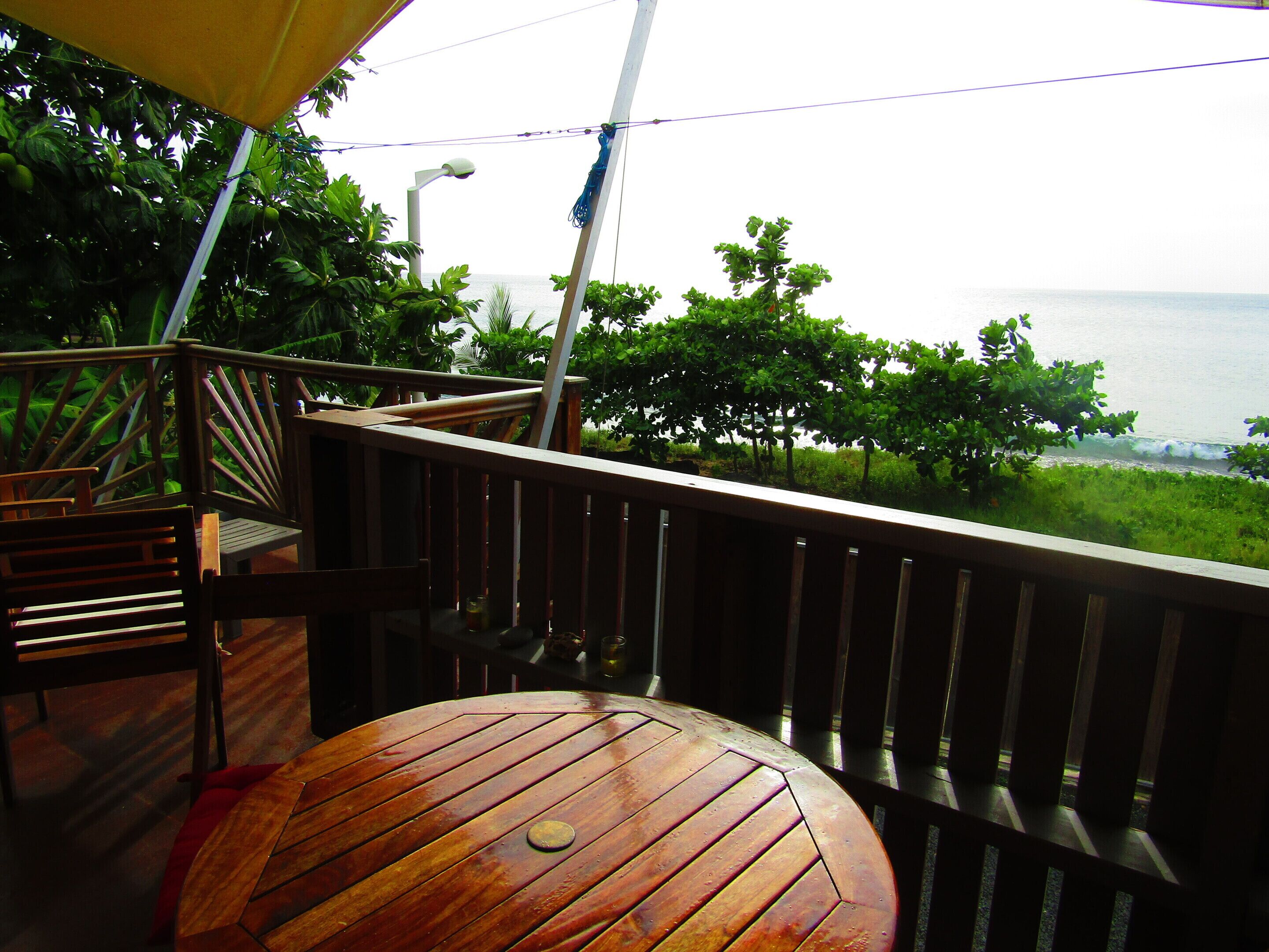 A wooden deck with a round table and chairs, overlooking a body of water and greenery.
