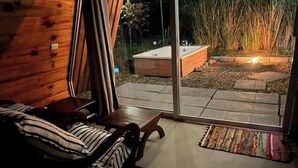 Une pièce chaleureuse avec un lit en bois, une petite table et une grande porte-fenêtre coulissante donnant sur un espace extérieur agrémenté d’un jacuzzi et de plantes.