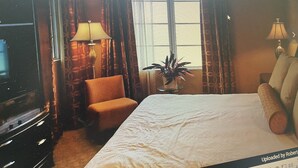 Ein Hotelzimmer mit Bett, Sessel, Fernseher, Lampe und Fenster.