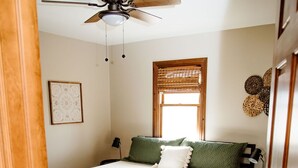 Ein Schlafzimmer mit Bett, Holzboden, Deckenventilator, Fenster mit Jalousien und einer Tür.