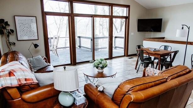 Ein Wohnzimmer mit einem braunen Ledersofa, einem Holztisch und einem an der Wand befestigten Fernseher.