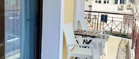 A balcony with a glass door, a table with chairs, and an air conditioning unit.