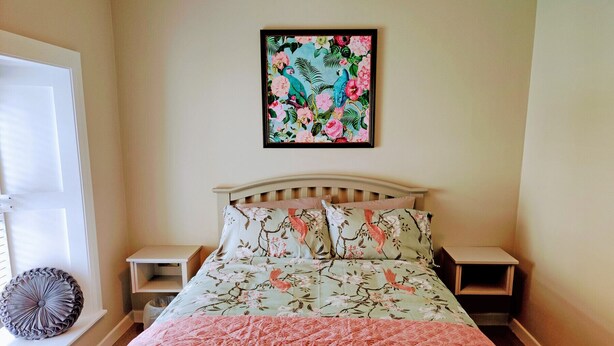 A bedroom with a bed, two bedside tables, a decorative pillow, and a framed floral artwork on the wall.