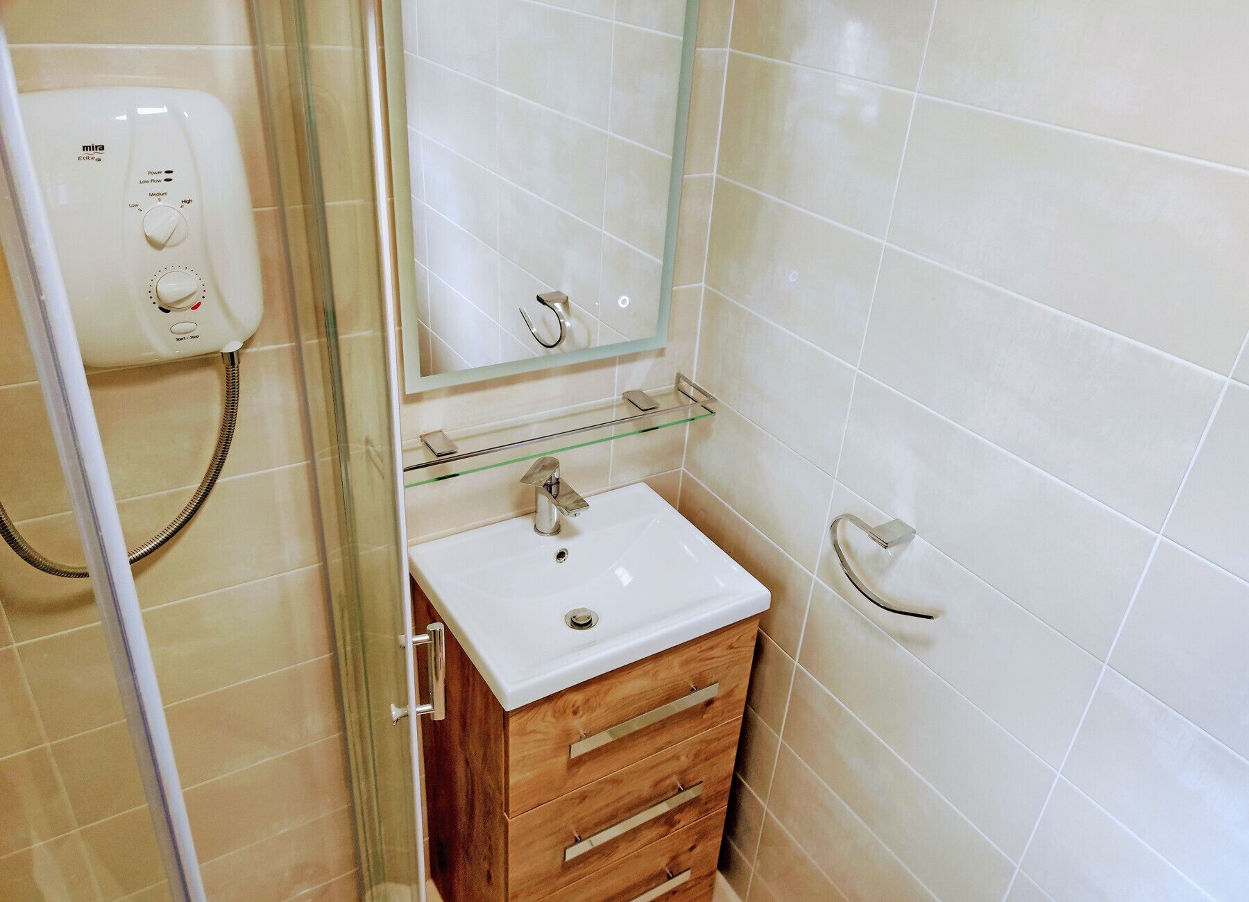 Un baño con lavamanos blanco, mueble de madera y cabina de ducha con mampara de vidrio.