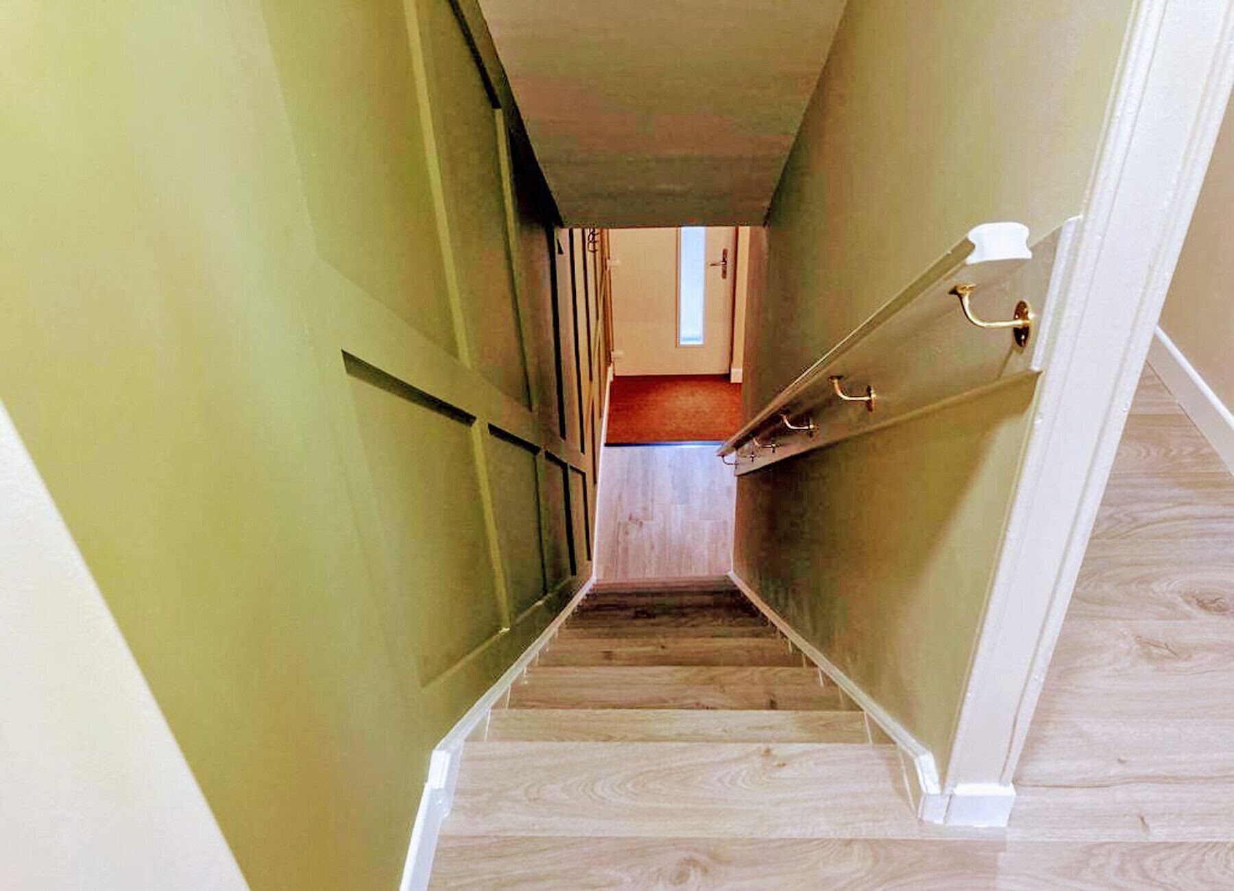 Een smalle gang met houten vloeren en groene wanden, die leidt naar een kamer met een deur en een klein raam.