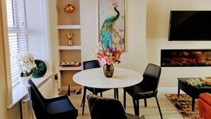 A dining area with a round table, chairs, a vase with flowers, a peacock painting, a TV, and a fireplace. - Tralee Townhouse Holiday Home (Tralee)