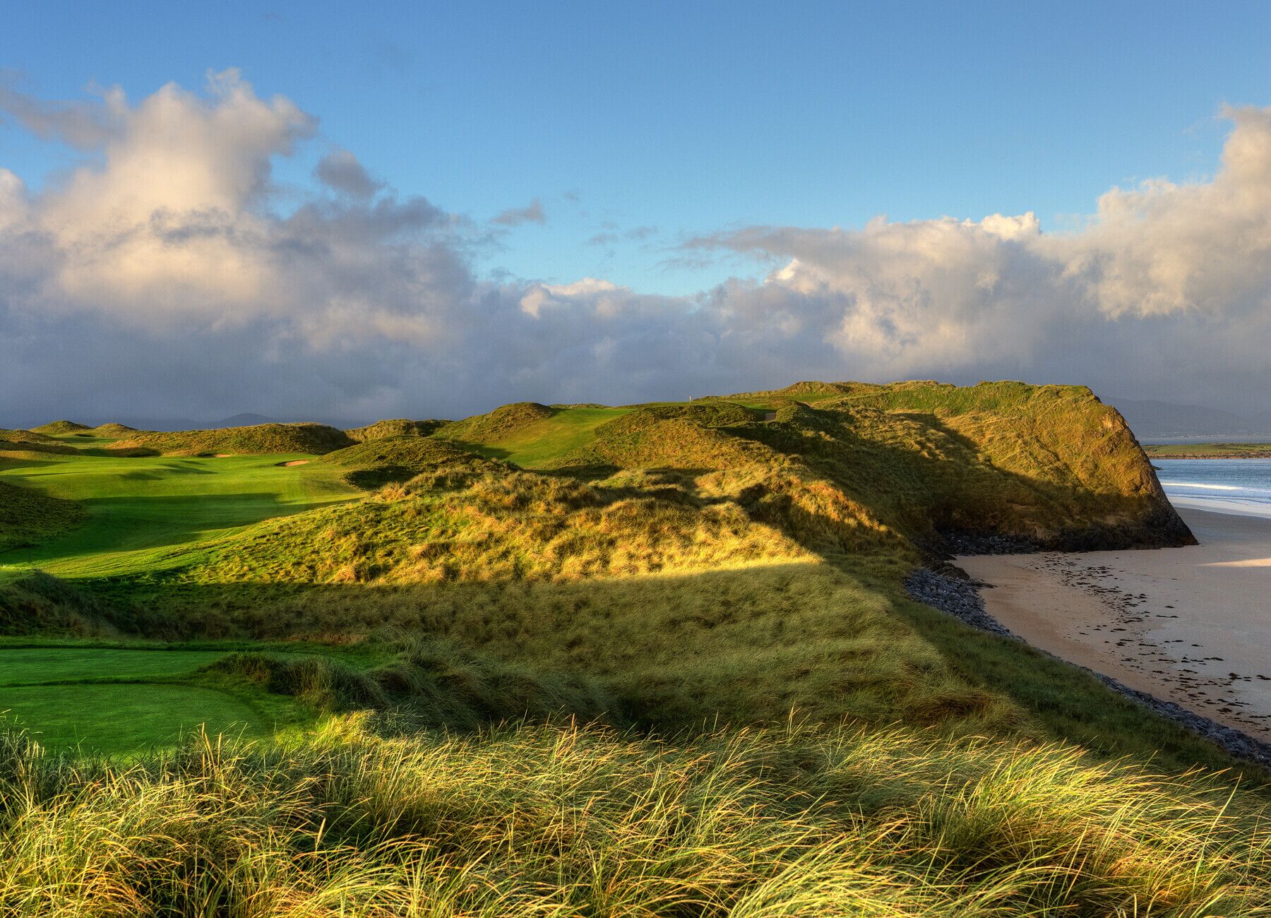 A coastal landscape with rolling hills, a beach, and a golf course.