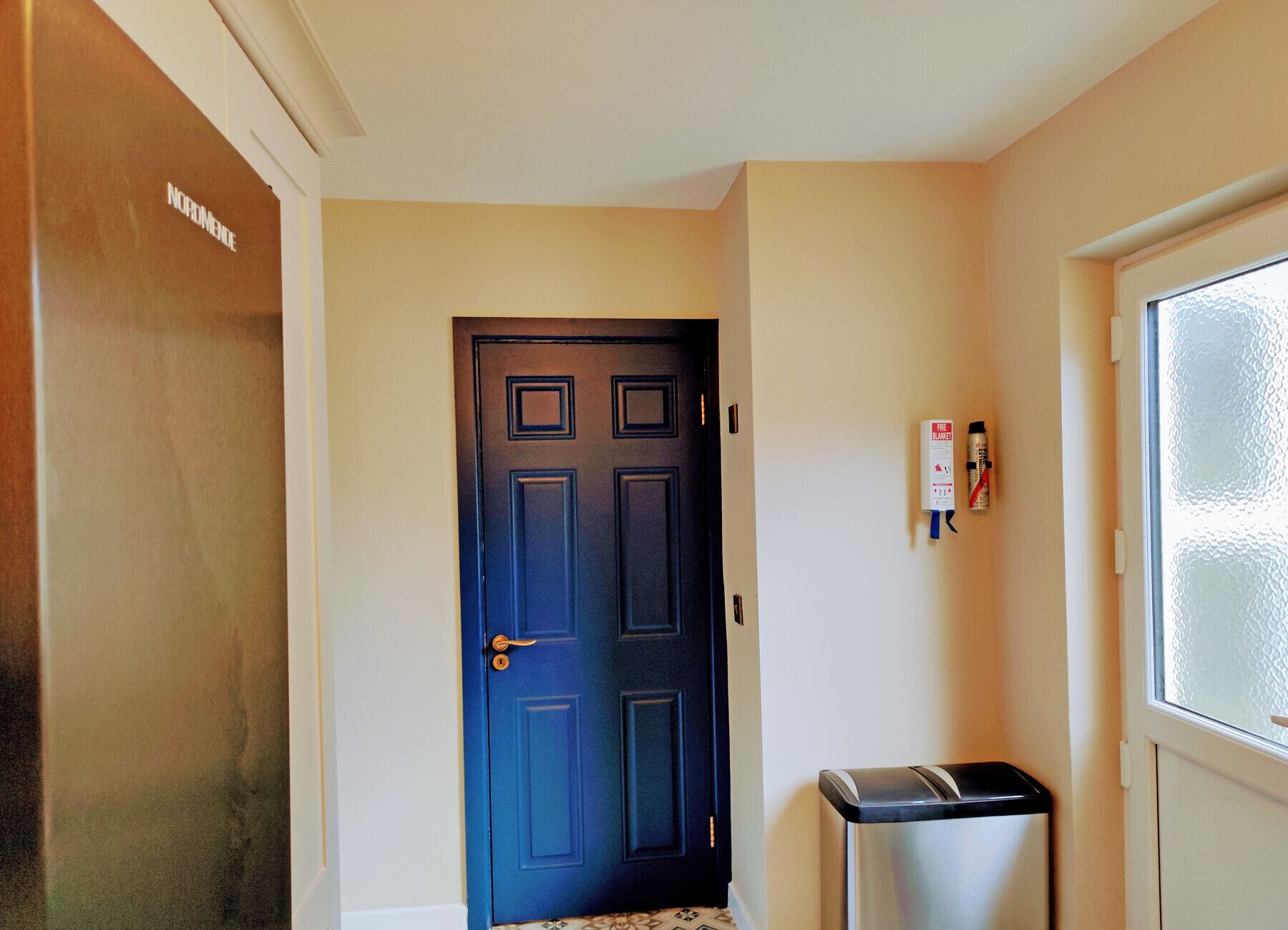 A hallway with a dark blue door, a trash bin, and a fire extinguisher on the wall.
