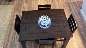 Uma sala de estar com um sofá marrom escuro, uma mesa de centro, uma mesa de jantar com cadeiras, uma televisão e um ventilador de teto.
