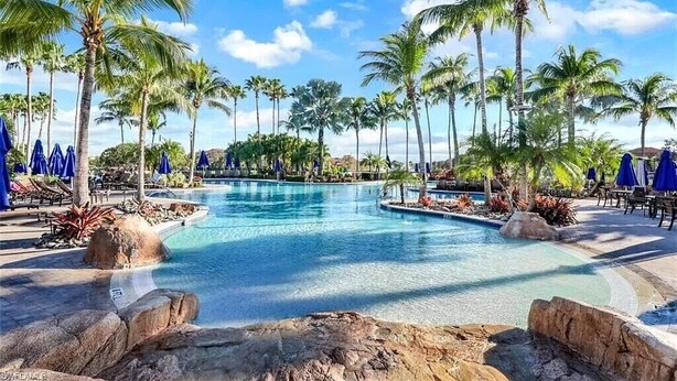 Uma área de piscina com palmeiras, espreguiçadeiras e guarda-sóis.