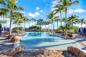 A pool area with palm trees, lounge chairs, and umbrellas.
