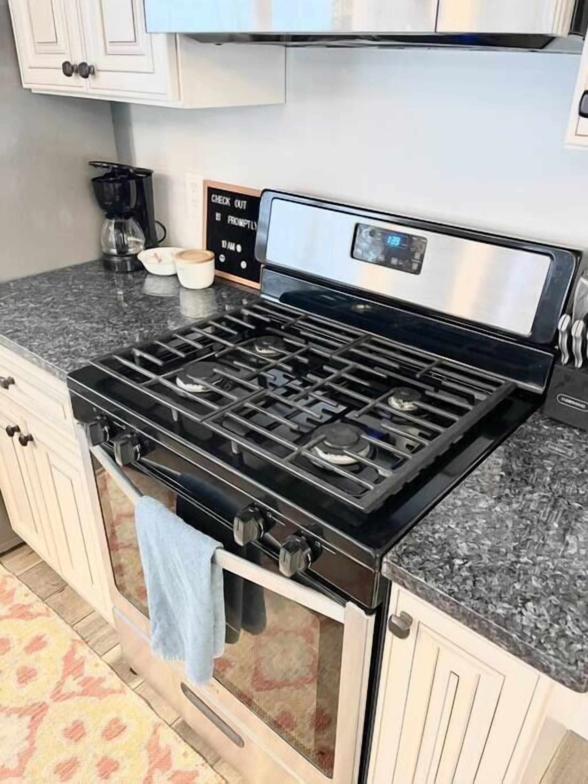 A kitchen with a gas stove, a coffee maker, and a check-out sign.