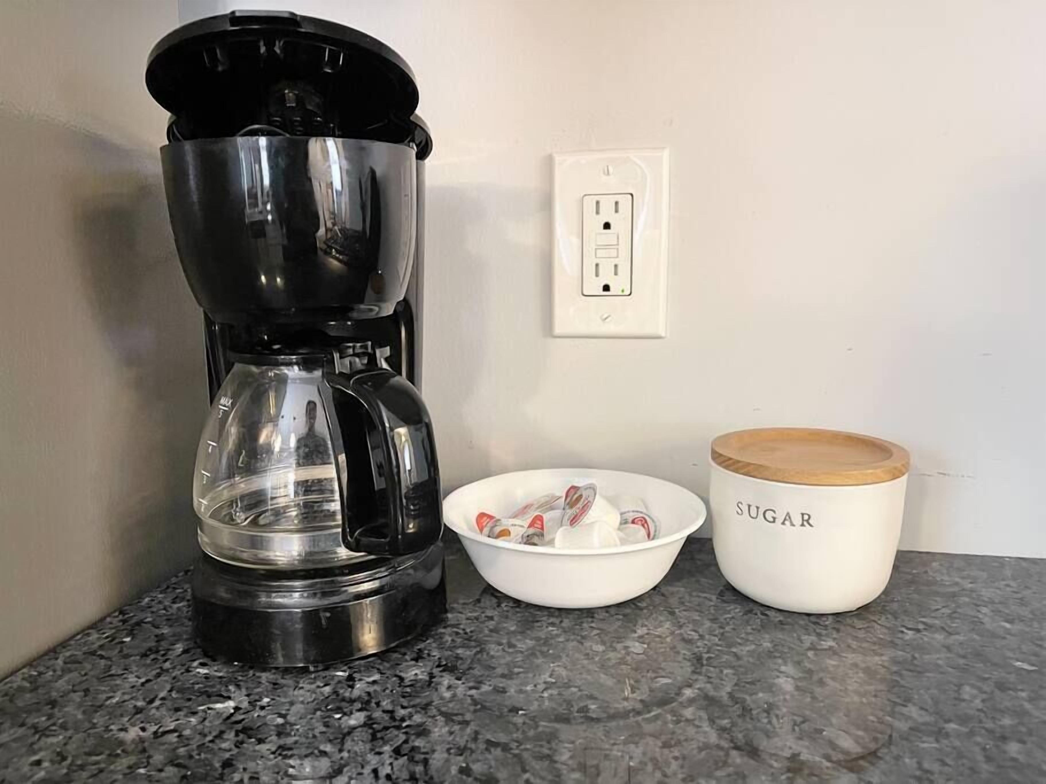 Une machine à café, un bol de sucre et un récipient à sucre sur un plan de travail de cuisine.