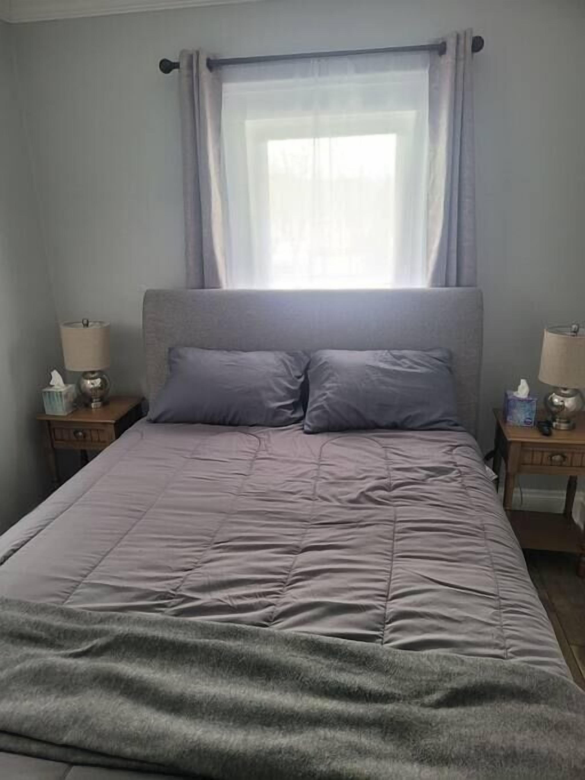 A bedroom with a bed, two bedside tables, a window with curtains, and a lamp on each table.