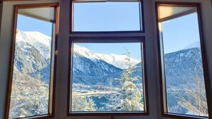 Une pièce dotée de trois grandes fenêtres donnant sur des montagnes enneigées et une vallée.