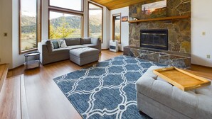 Un salon moderne doté d’une cheminée en pierre, de grandes fenêtres offrant une vue sur les montagnes et d’un coin salon confortable.